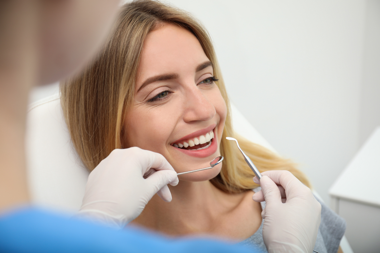 Smiling woman at a dental check-up, dentist’s gloved hands holding dental tools near her mouth. The setting is bright, conveying a calm atmosphere. Smiling woman at a dental check-up, dentist's gloved hands holding dental tools near her mouth. The setting is bright, conveying a calm atmosphere.
