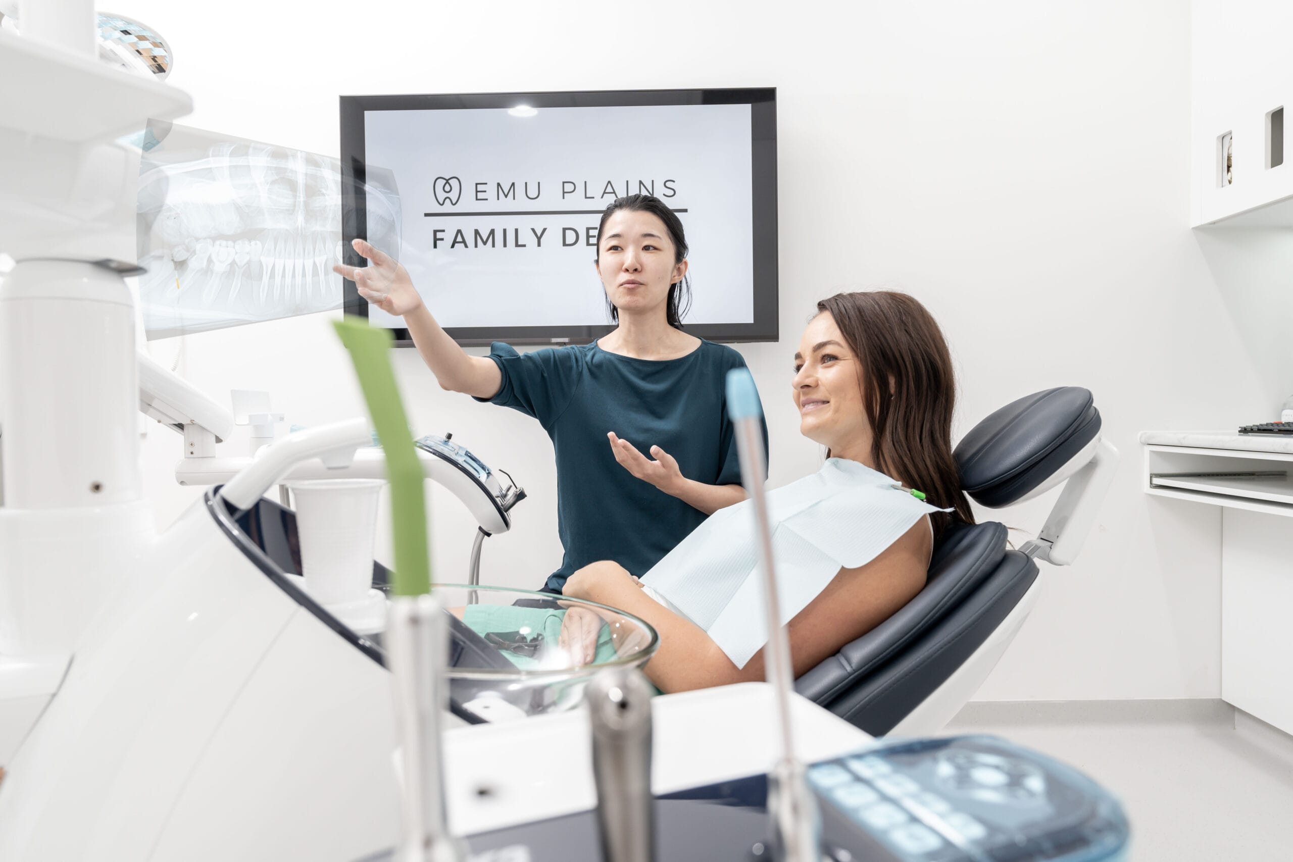 A dentist explaining an X-ray to a patient in a modern dental office. The patient, smiling and relaxed, is seated in a dental chair.