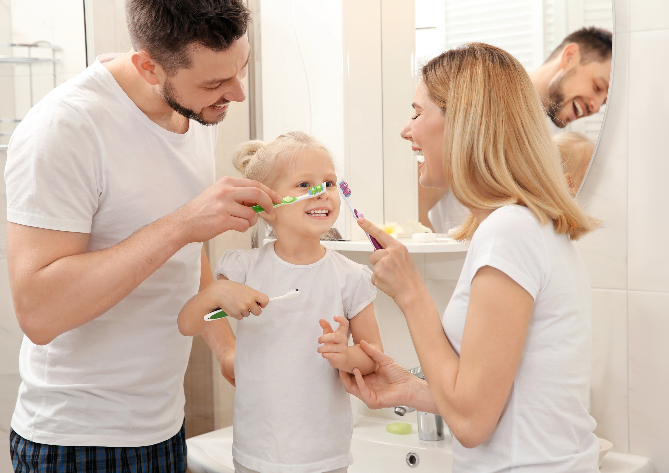 Family in a bathroom wearing bathrobes, two parents helping a young boy and girl brush their teeth, creating a joyful and nurturing atmosphere.