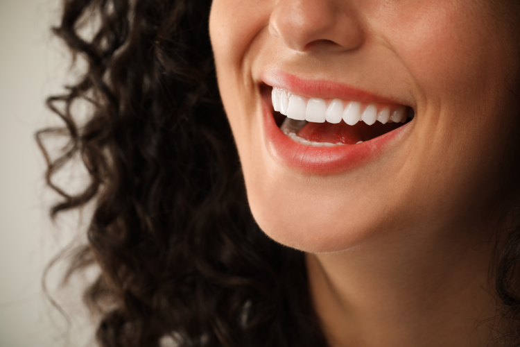 A woman with curly hair smiles widely, showing bright white teeth. The image captures a sense of joy and positivity, focusing on her mouth and lower face. A woman with curly hair smiles widely, showing bright white teeth. The image captures a sense of joy and positivity, focusing on her mouth and lower face.