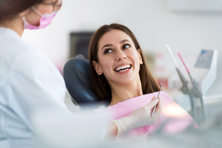 Understanding the benefits of preventative family dentistry A woman smiles while seated in a dentist's chair, looking at the dentist holding a dental tool. The atmosphere is friendly and reassuring.