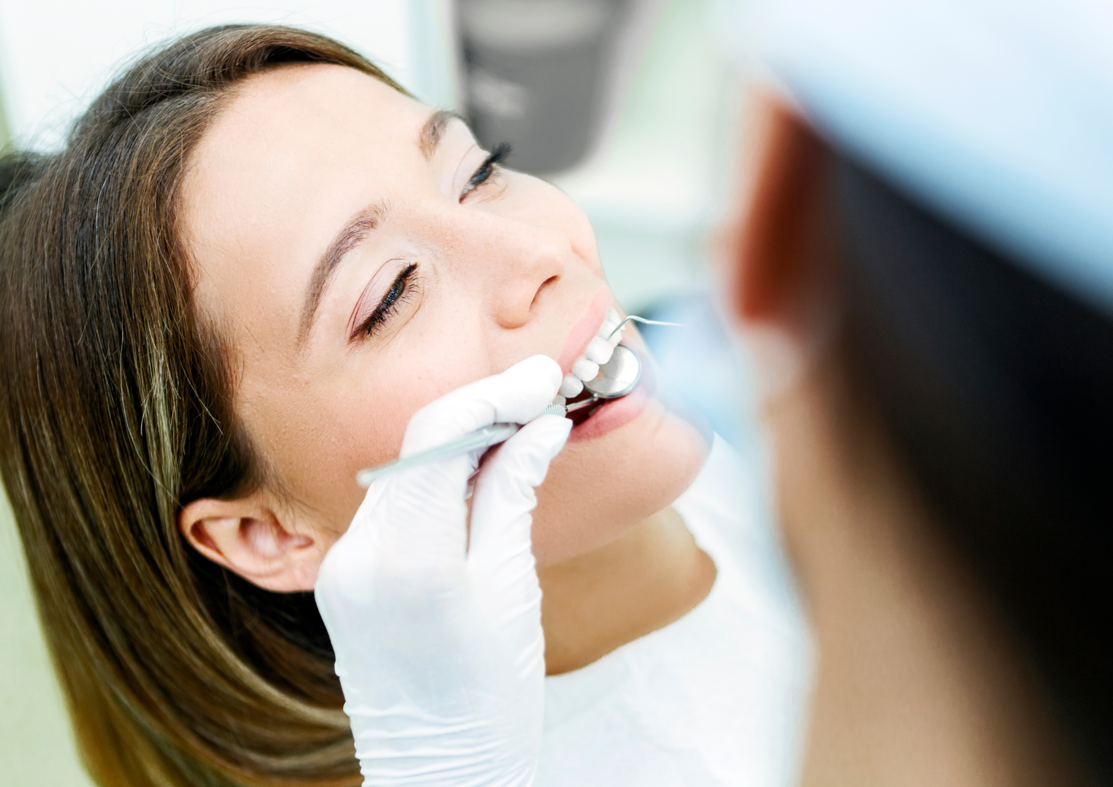 Emu-Plains-Family-Dentistry-Dental-Checkup A woman smiles while receiving dental care. A dentist in gloves uses a dental mirror and tool, creating a calm and professional atmosphere.