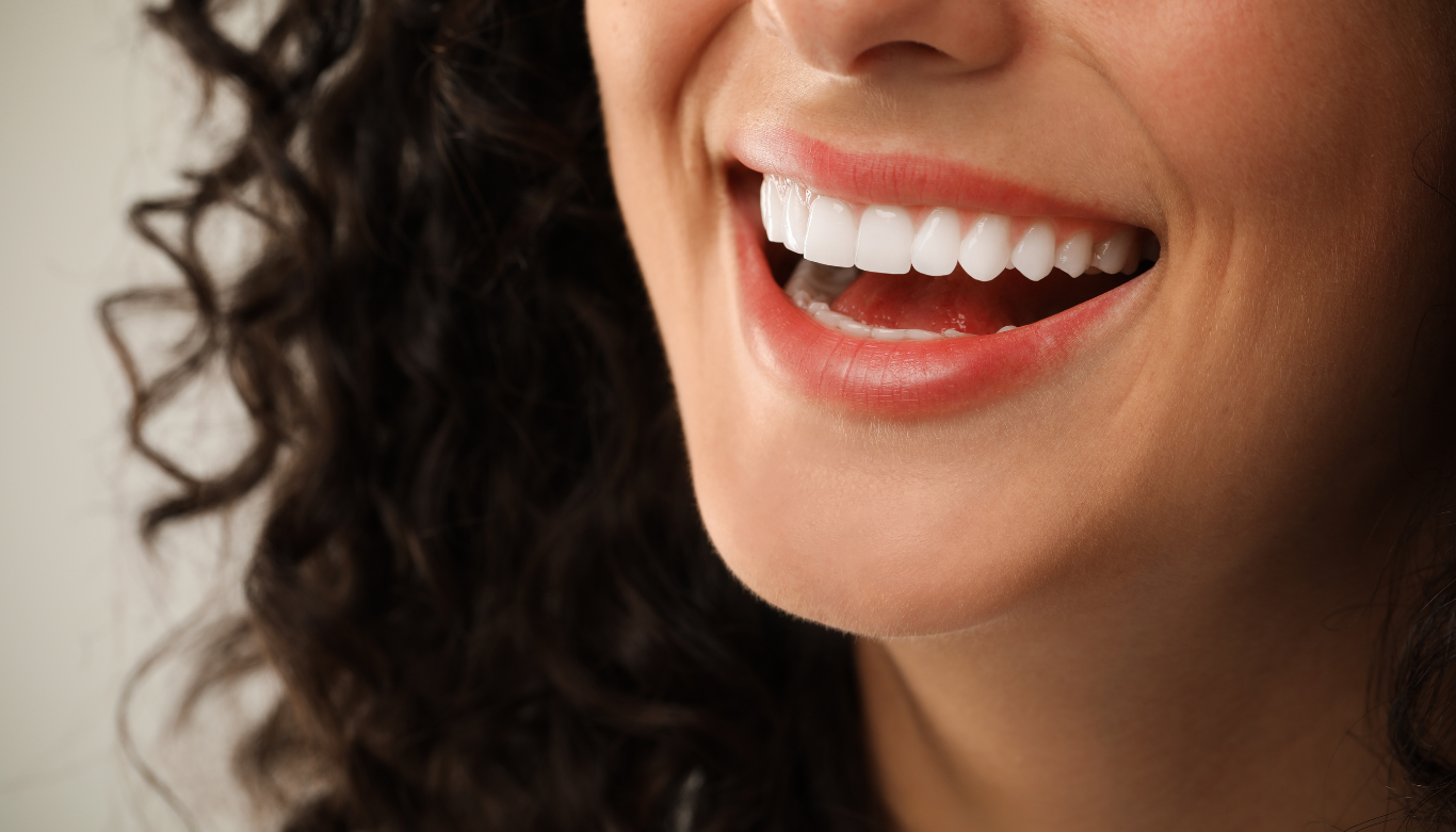 Dental Blog Images 3 Close-up of a person smiling with curly hair visible, showcasing white teeth and red lips. The image conveys joy and warmth.