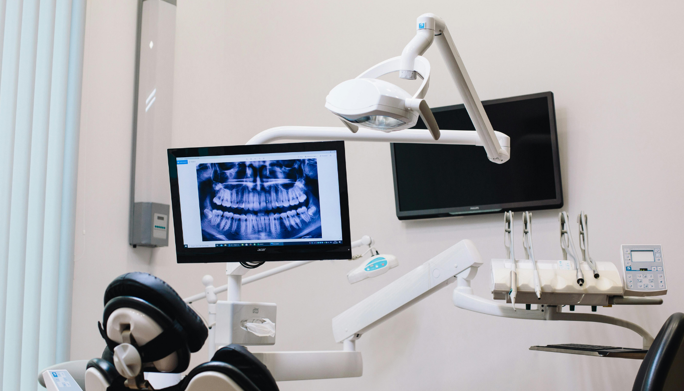 emu-plains-family-dental-cheap-dentist-near-me Dental exam room with a monitor showing a panoramic X-ray of teeth beside a chair and overhead light.