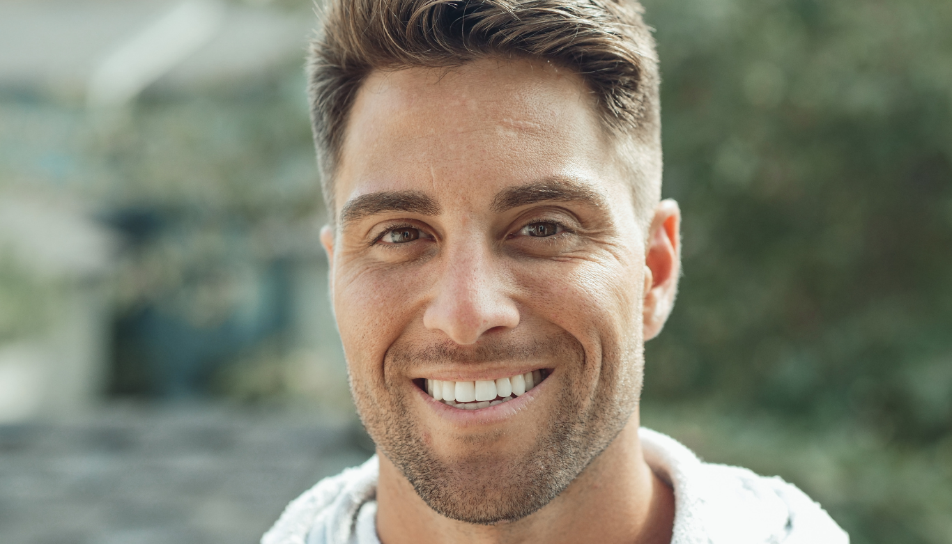 emu-plains-family-dental-gum-surgery-dentist Close-up portrait of a smiling man with short brown hair outdoors, wearing a light hoodie/sweater.
